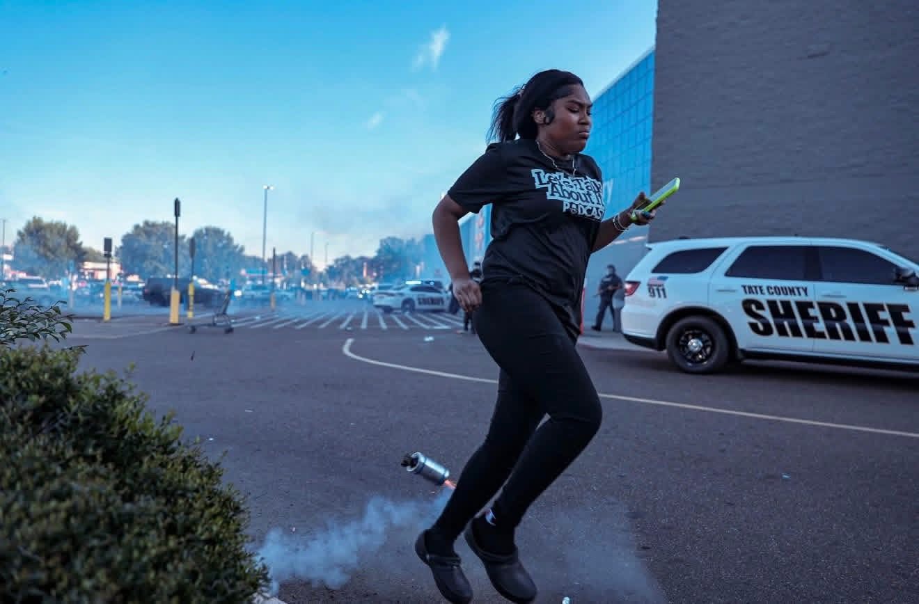 A woman runs from tear gas near a sheriff's vehicle